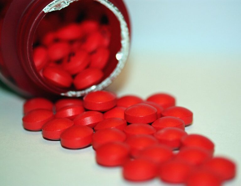 Compresse rosse fuoriescono da un flacone di medicinali