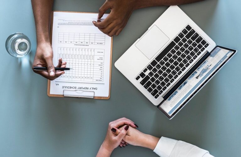 Mani di un medico su una scheda clinica accanto a un computer portatile con dati sanitari
